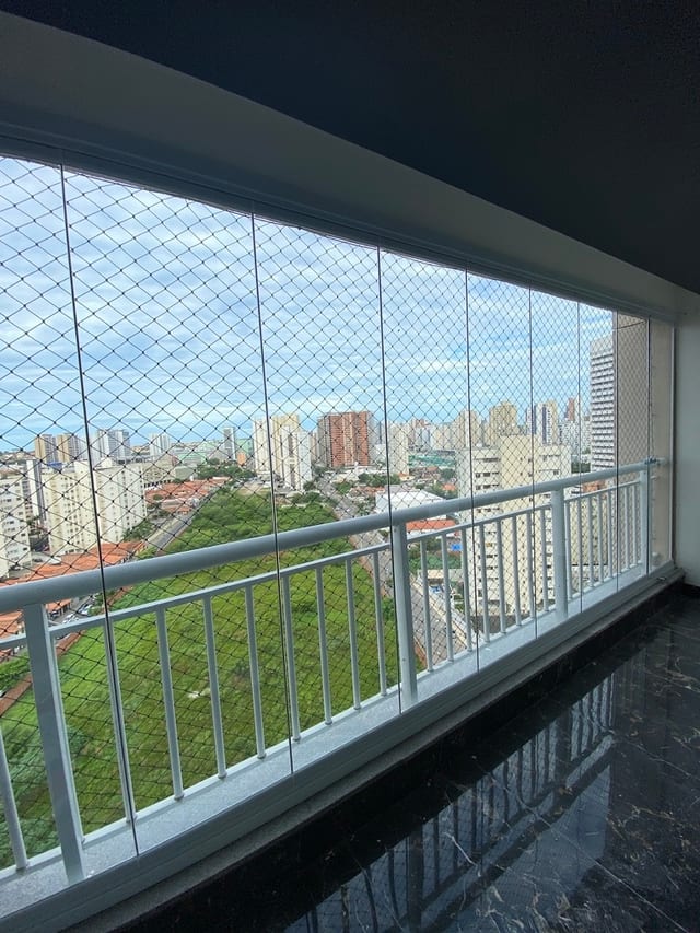 Varanda curva fechada com cortina de vidro, tela de proteção e vista para os prédios em dia nublado