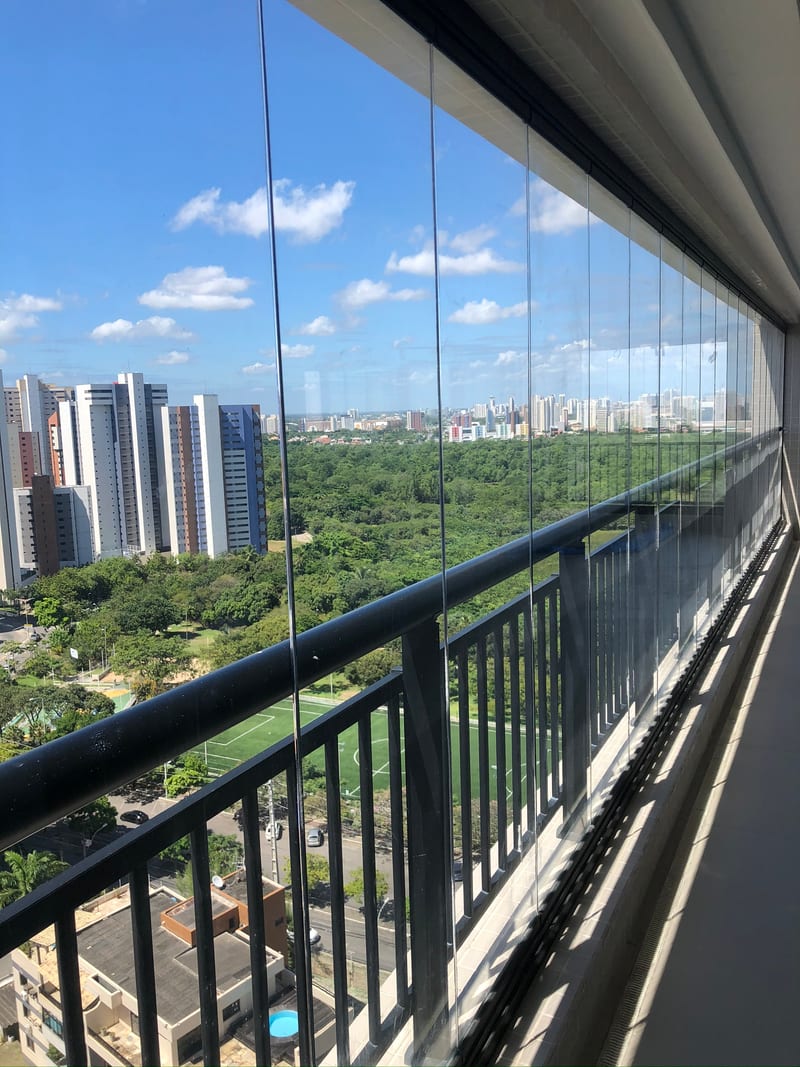 Varanda envidraçada em andar alto com vista para área verde e para os prédios de Fortaleza